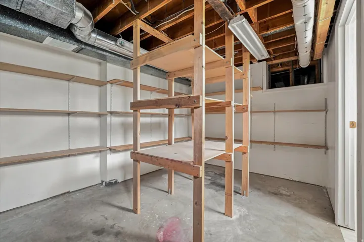 Expansive utility space featuring concrete flooring, built-in shelving, exposed ceiling joists, and ductwork