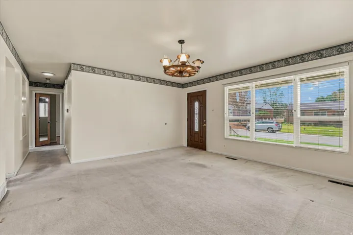 Spacious room featuring light-colored carpeting and a chandelier-style lighting fixture