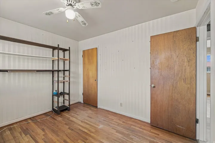 Wood-finish flooring, white beadboard-style wall paneling, and a ceiling fan with integrated lighting