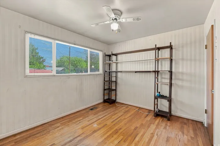 Hardwood flooring, horizontal window with blinds, ceiling fan, and built-in shelving
