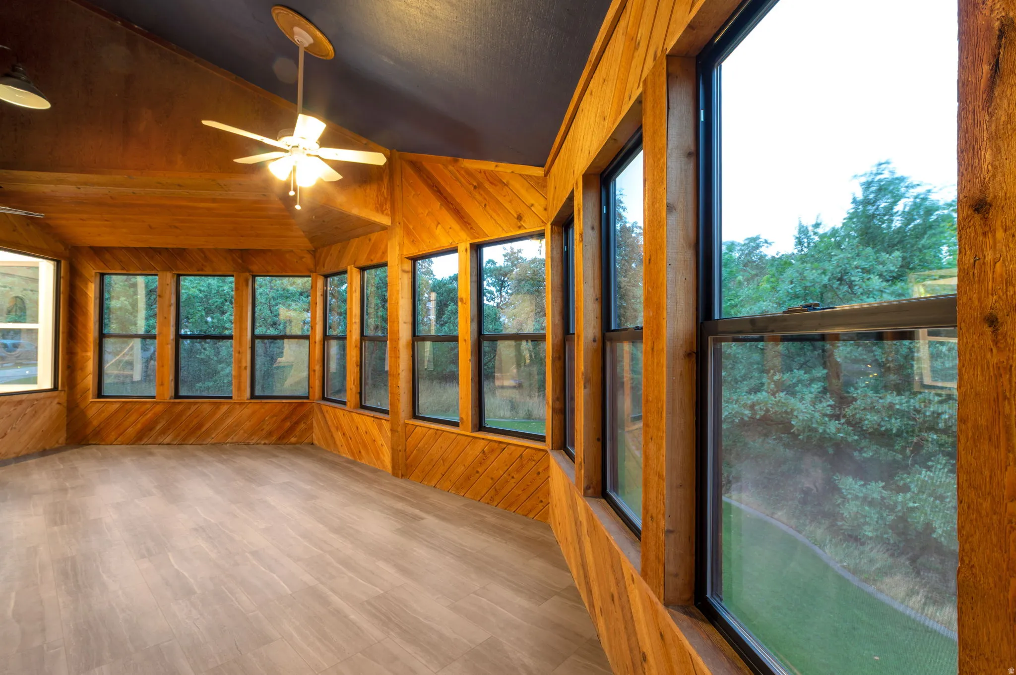 This Sunroom or Den has wraparound windows, wood-paneled walls, LVP flooring, and a ceiling fan. It also has its own door out to the wrap around deck!