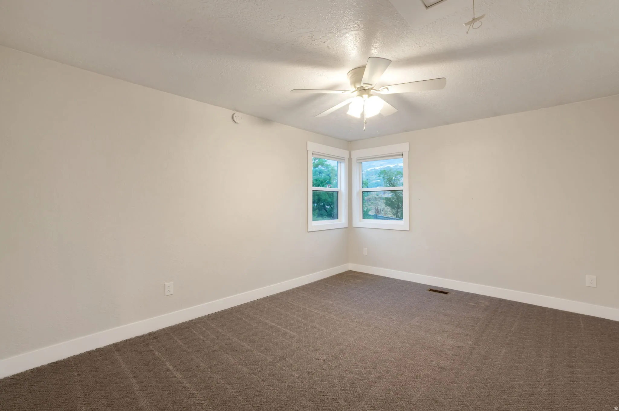 Carpeted room with a ceiling fan, two windows with white trim, and light-toned walls
