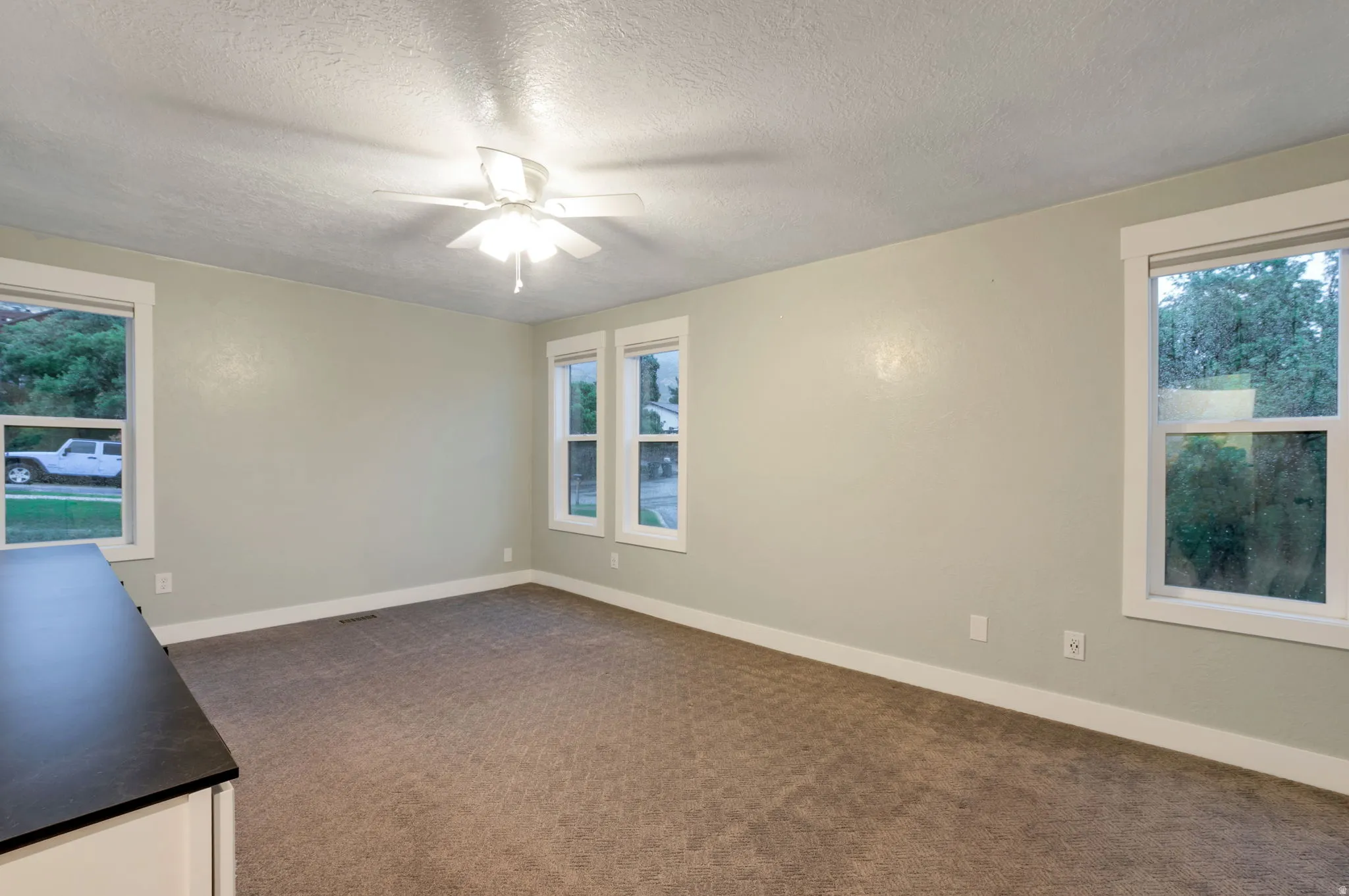 Master bedroom with soft neutral wall color, textured carpeting, multiple windows, and a ceiling fan with integrated lighting
