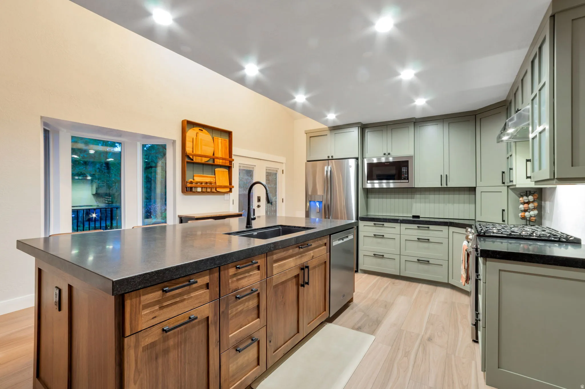 Kitchen featuring a large island with dark countertop, light green cabinetry, stainless steel appliances, and light wood-finish flooring