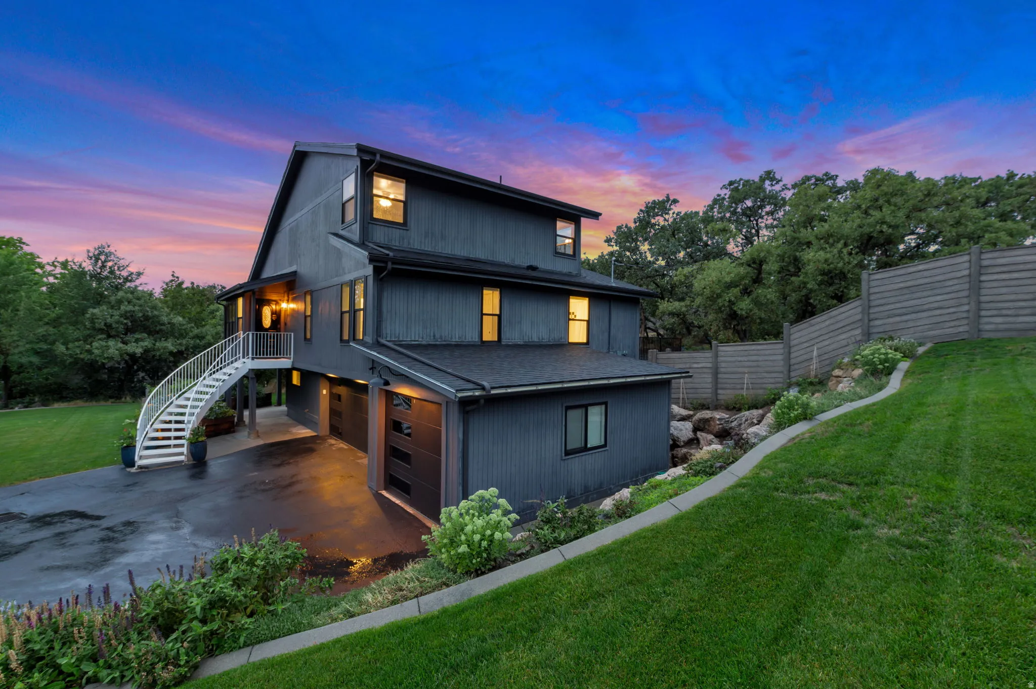 Multi-level exterior with dark siding, arched outdoor staircase, and an attached three-car garage