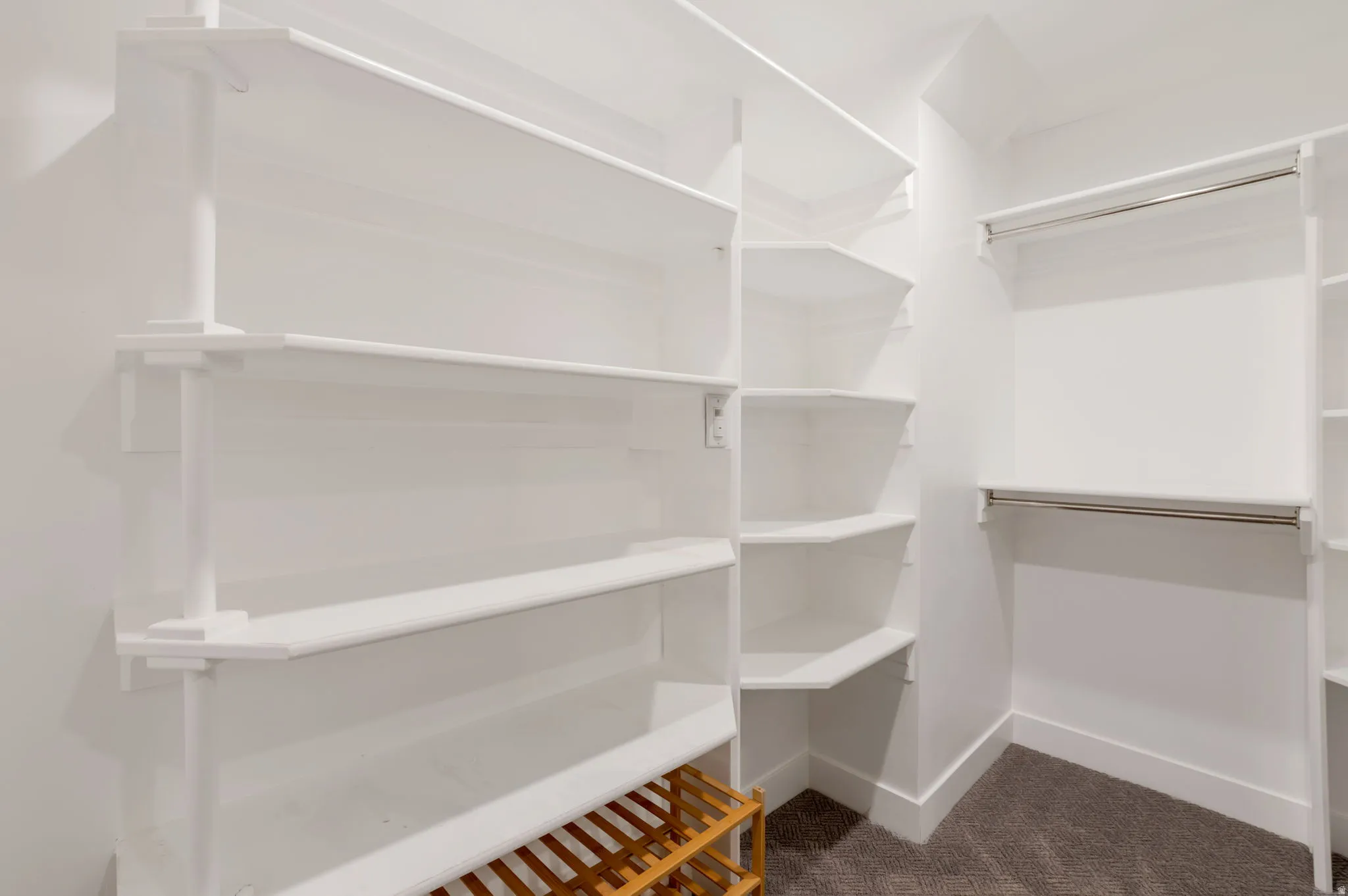 Custom walk in master closet system with multiple shelving units, corner shelving, and dual hanging rods, set against white walls and carpet flooring