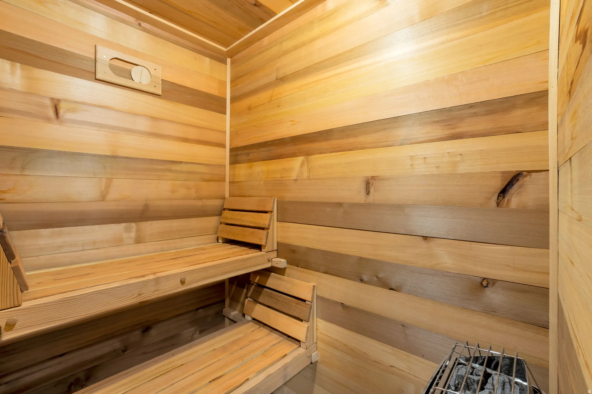 Sauna featuring horizontal Cedar wood wall paneling, tiered bench seating with adjustable backrests, and integrated ventilation.
