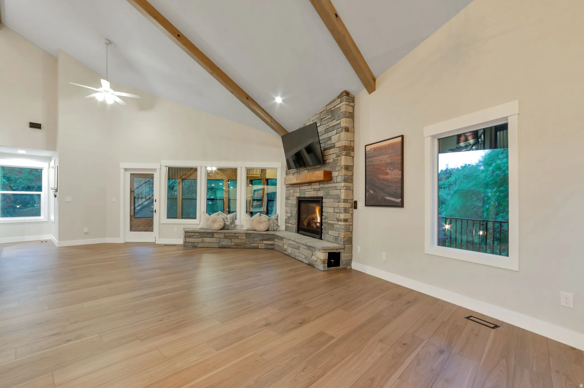 Vaulted ceiling with exposed wood beams, stone-clad fireplace with mantel, built-in stone bench seating, and expansive windows
