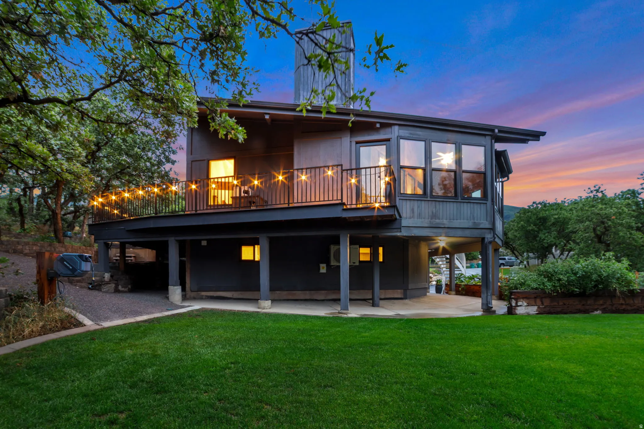 Contemporary exterior with dark siding, expansive elevated deck with metal railings, large picture windows, and a manicured lawn