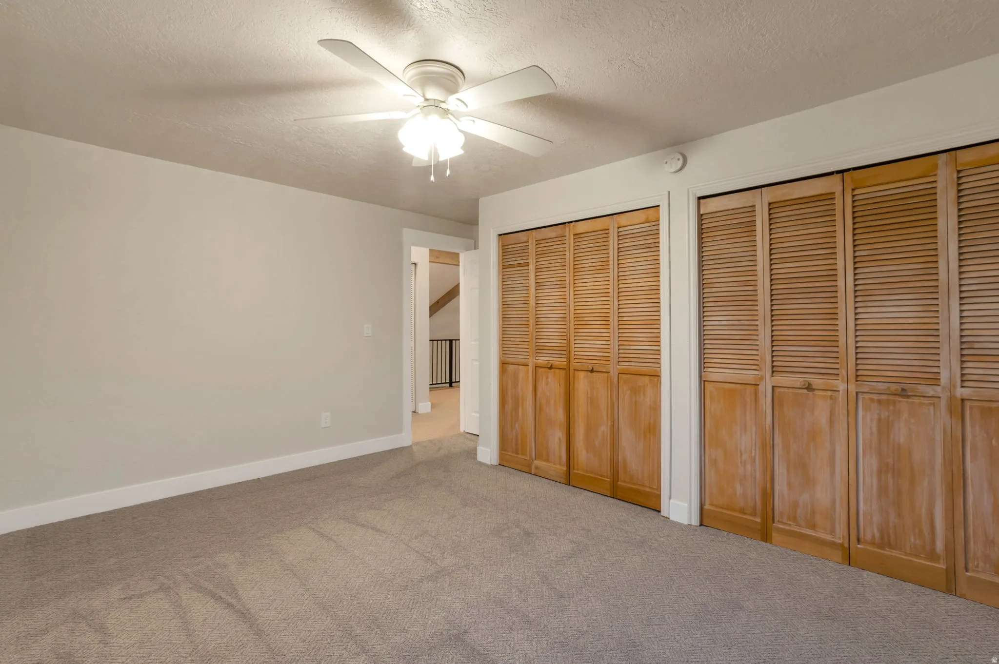 Neutral wall paint, ceiling fan with light fixture, carpeted flooring, and two sets of bi-fold louvered closet doors