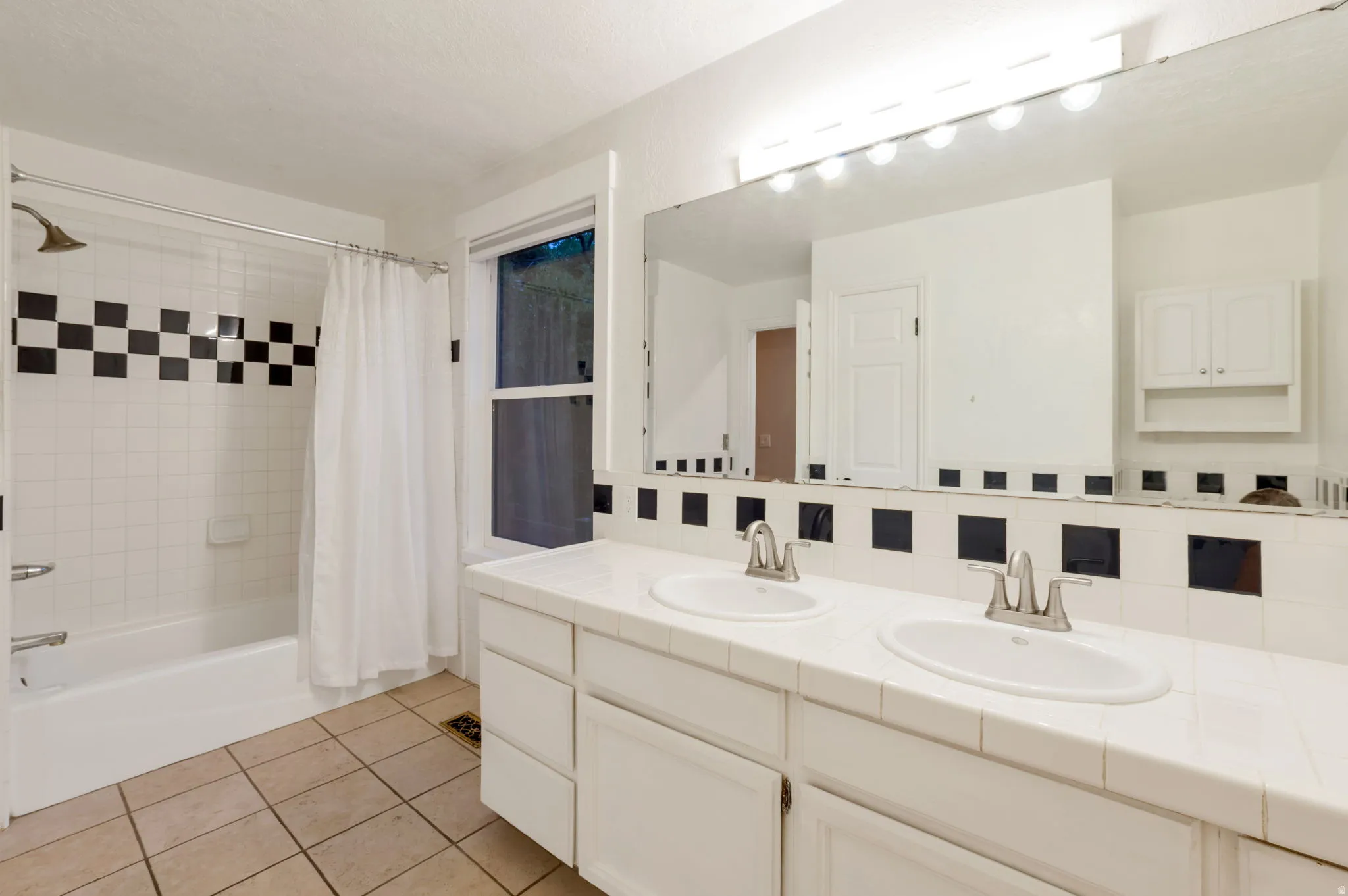 Bathroom featuring a shower tub, double vanity with integrated sinks, tile countertop, and white cabinetry