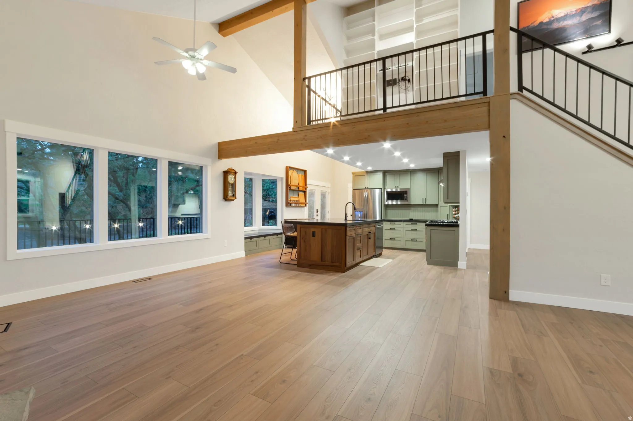 Vaulted ceiling with exposed wood beams, large windows, kitchen with green cabinetry, and a loft with built-in shelving