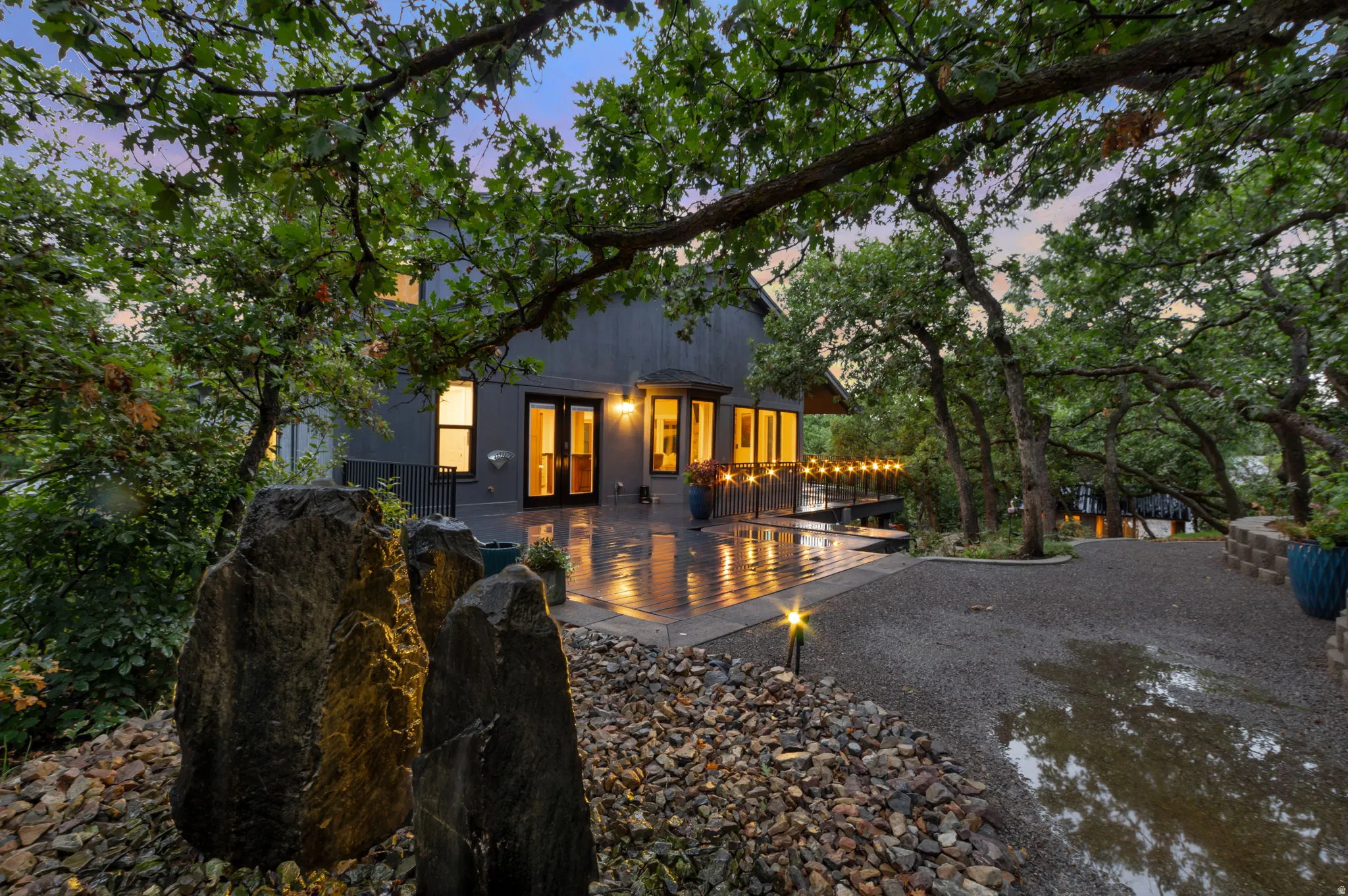 Expansive outdoor deck with string lighting, beautiful natural stone fountain surrounded by mature trees