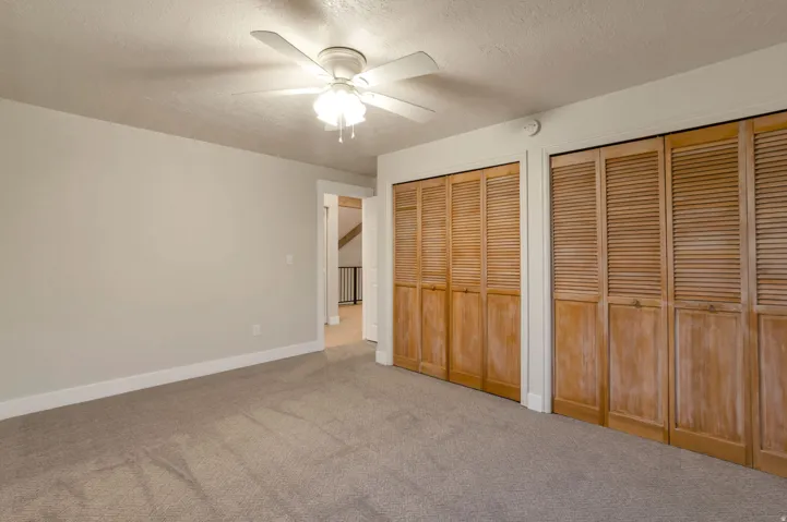 Neutral wall paint, ceiling fan with light fixture, carpeted flooring, and two sets of bi-fold louvered closet doors