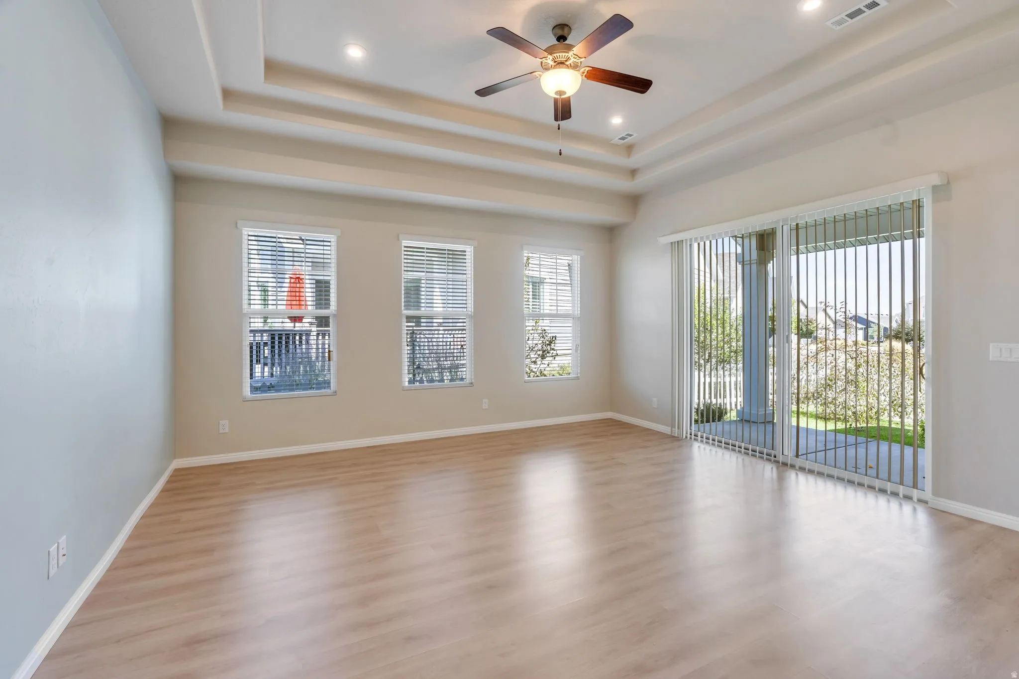 Tray ceiling with recessed lighting and a ceiling fan, wood-finish flooring, multiple windows, and a sliding glass door