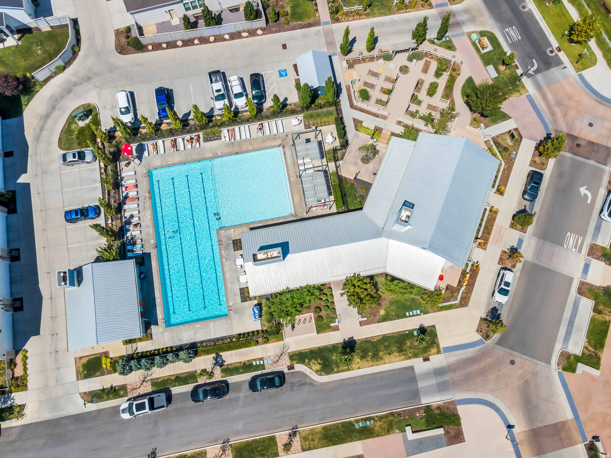 Outdoor swimming pool, paved parking areas, contemporary building with a metal roof, landscaped grounds, and a community garden