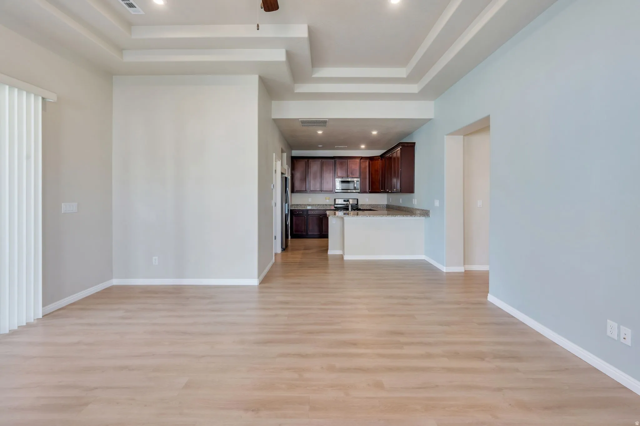 Tray ceilings with recessed lighting, wood-finish flooring, kitchen with dark wood cabinetry, stainless steel appliances, and a breakfast bar
