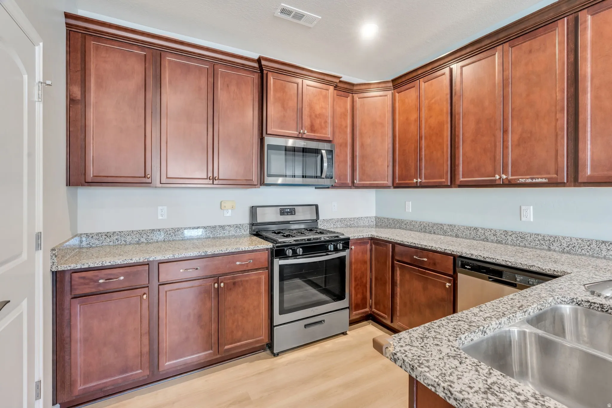 Kitchen featuring wood-finish cabinetry, light-toned countertops, and stainless steel appliances, including a range, microwave, and dishwasher