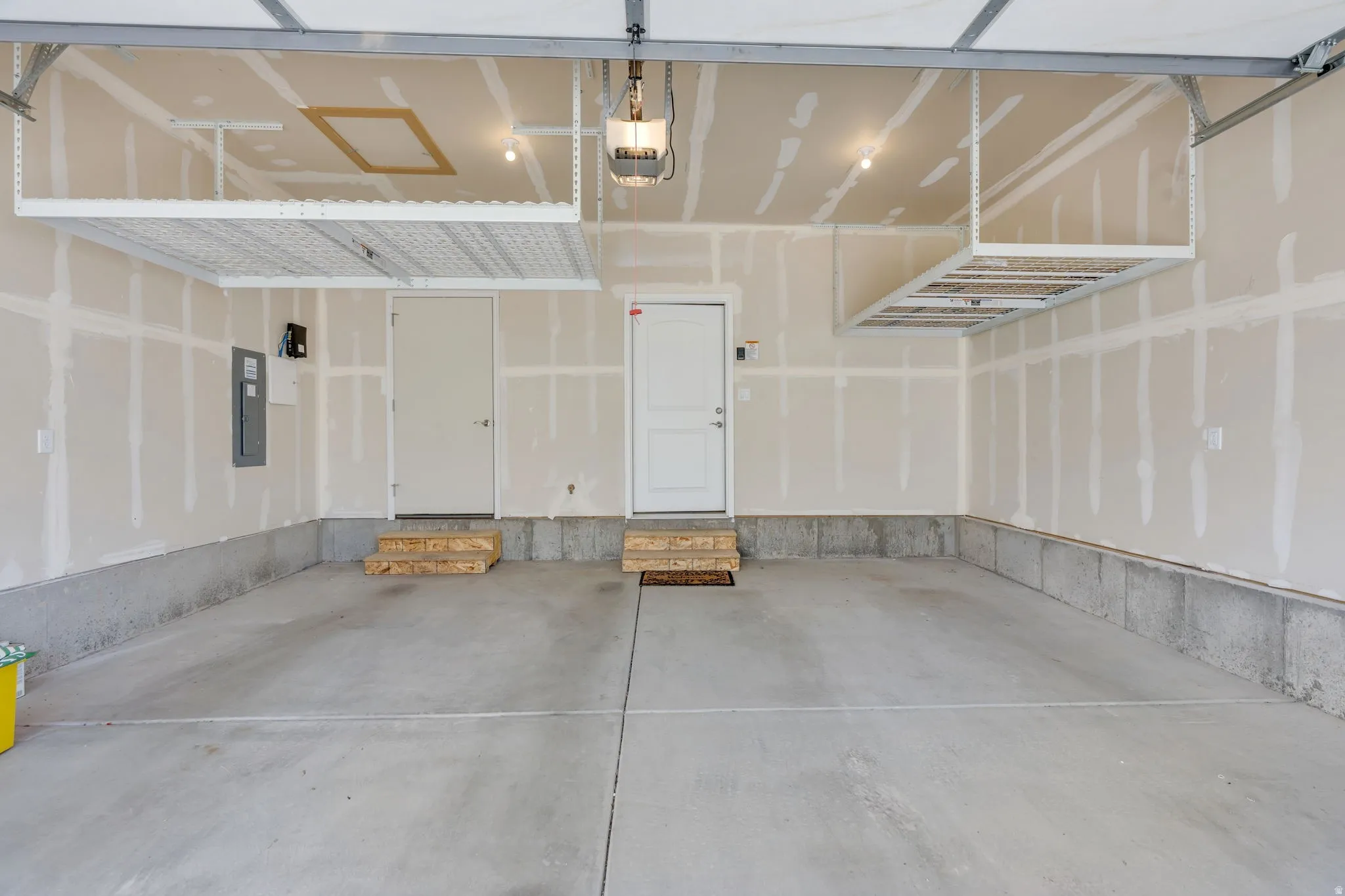 Concrete flooring, two interior access doors, overhead storage racks, exposed ceiling joists, and an overhead garage door track system