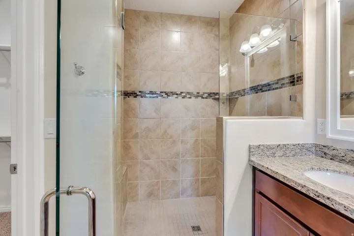 Walk-in shower with full-height tile surround, decorative mosaic tile accent, and glass enclosure