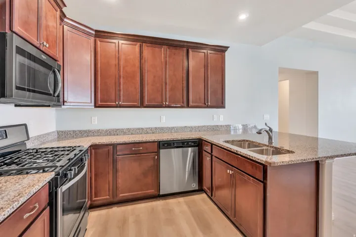 Kitchen featuring wood-finish cabinetry, speckled countertops, stainless steel appliances, and a double basin sink