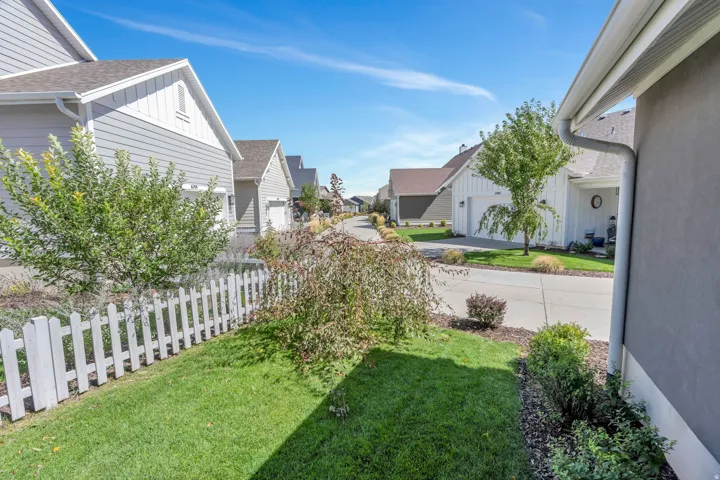 Manicured lawn with a white picket fence, mature landscaping, and an asphalt driveway