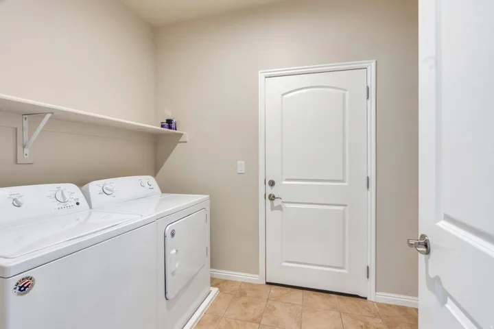Laundry area featuring a built-in shelving unit, a white paneled door, and tiled flooring