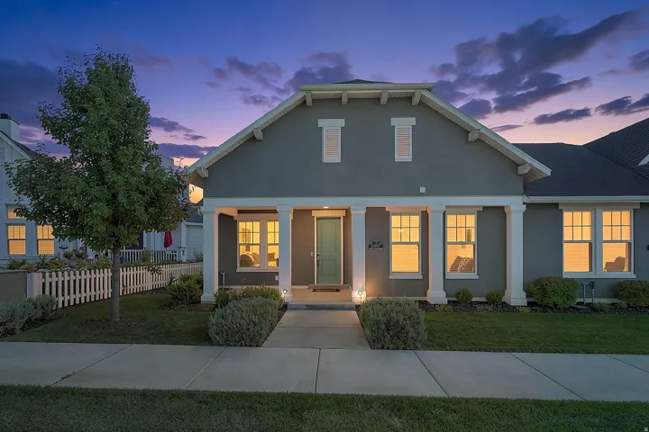 Gray stucco exterior with white trim, a covered entry porch supported by columns, and a light-colored front door