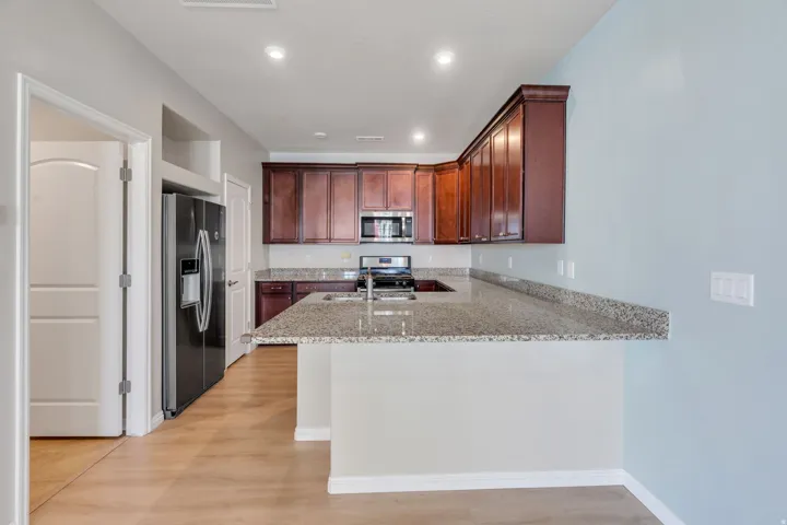 Wood-finish flooring with recessed lighting, dark wood cabinetry, stainless steel appliances, and light-toned countertops