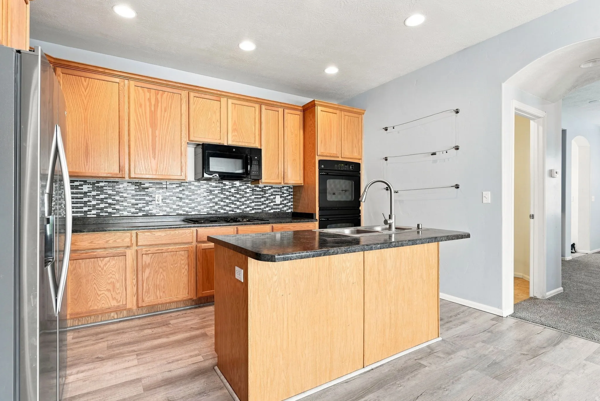 Kitchen featuring wood cabinetry, dark countertops, a mosaic tile backsplash, stainless steel refrigerator, and wood-finish flooring