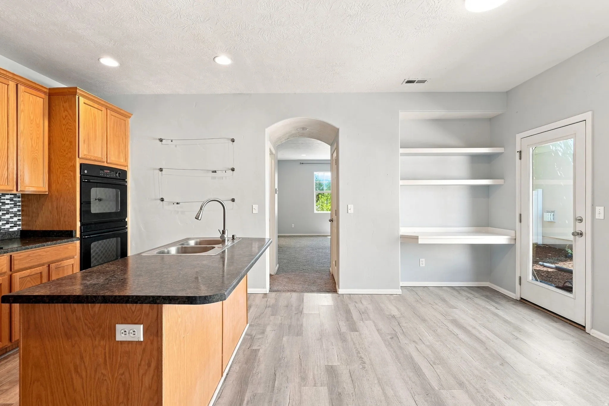 Kitchen featuring wood cabinetry, stainless steel double basin sink, double wall ovens, and a patterned tile backsplash