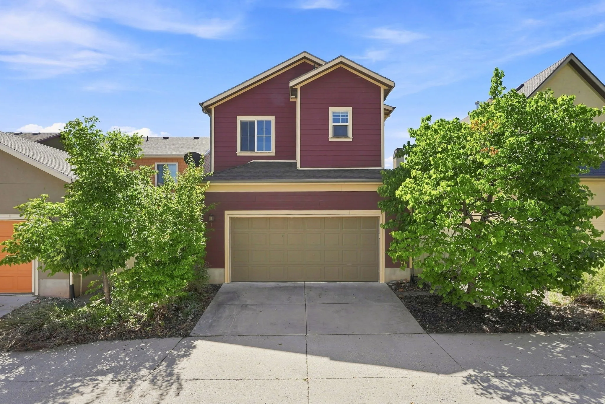 Two-story exterior with a rich red facade, featuring a prominent garage door, mature trees, and a concrete driveway