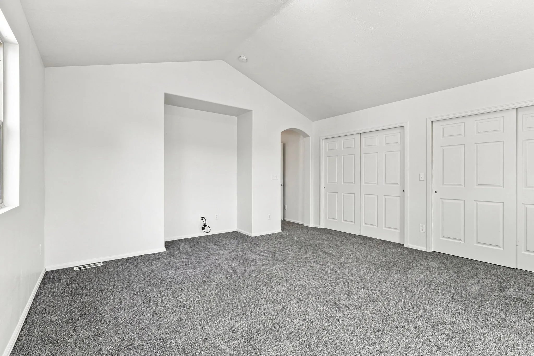 Vaulted ceilings, neutral carpet flooring, recessed wall niche, arched doorway, and white panel sliding closet doors