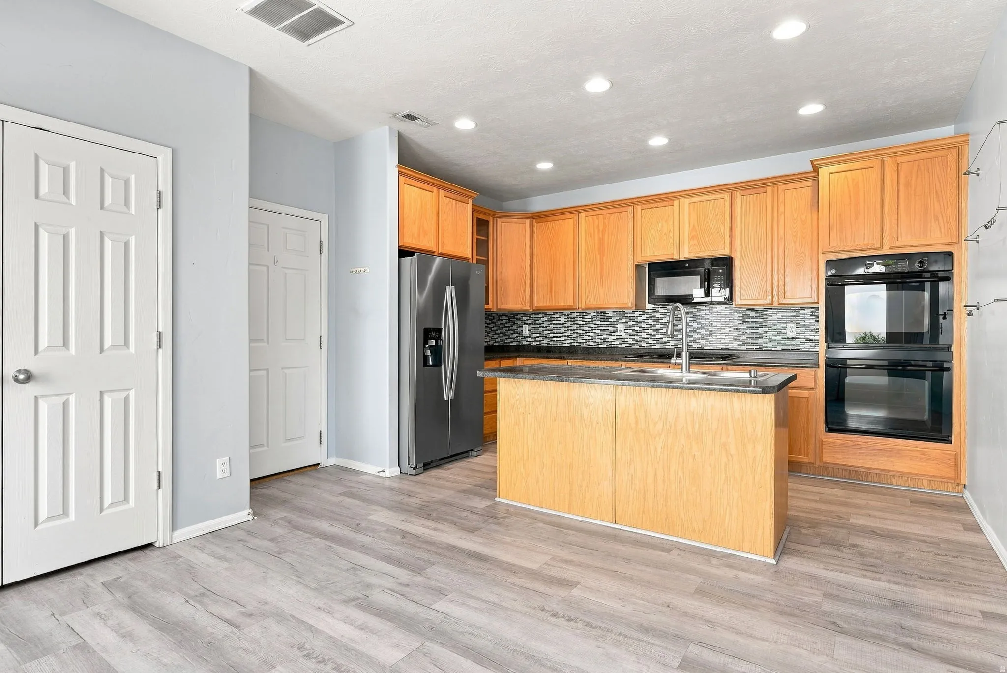 Kitchen featuring wood-finish flooring, recessed lighting, wood cabinetry, a tile backsplash, and stainless steel appliances
