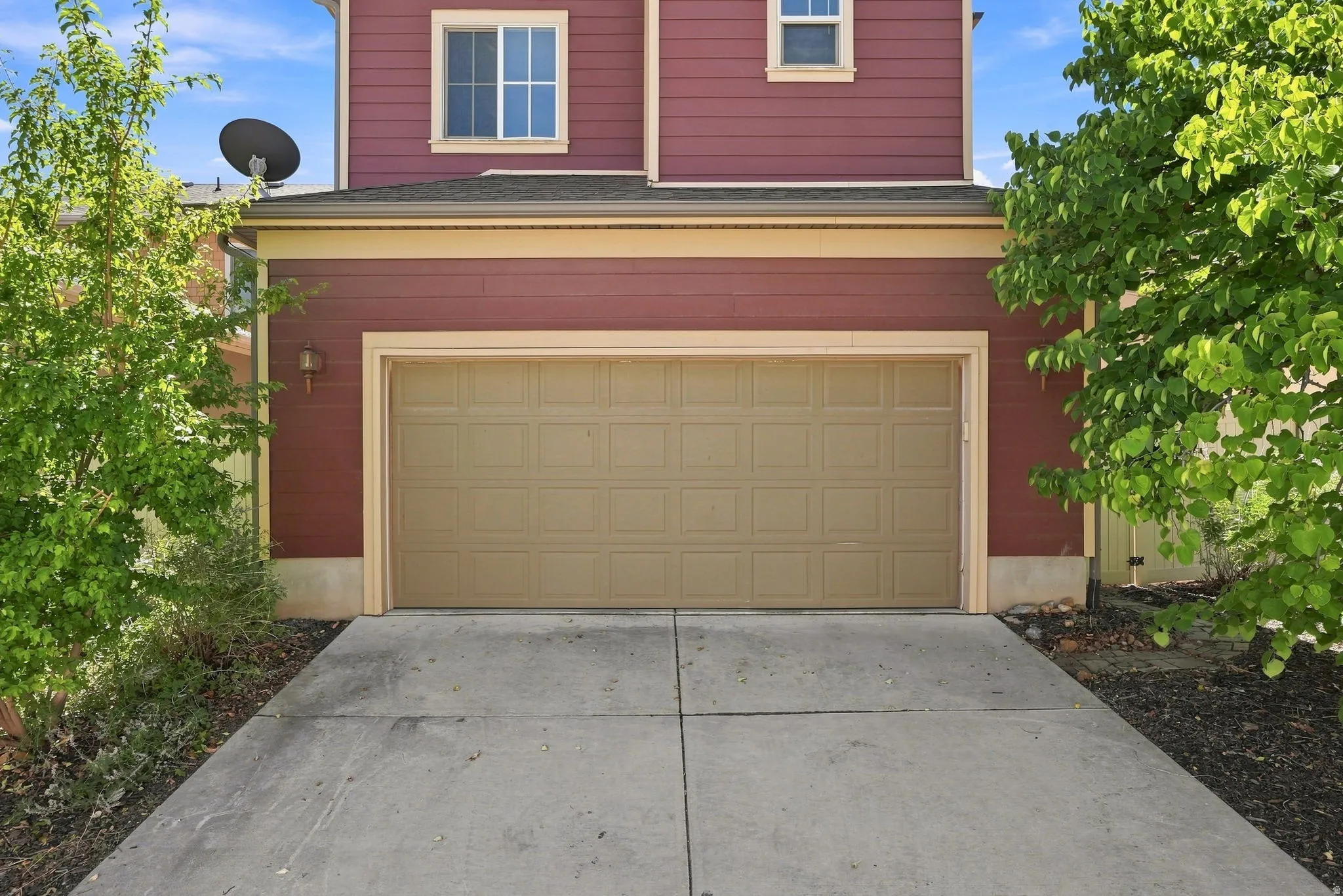 Red siding exterior with contrasting trim, single garage door, concrete driveway, and established landscaping