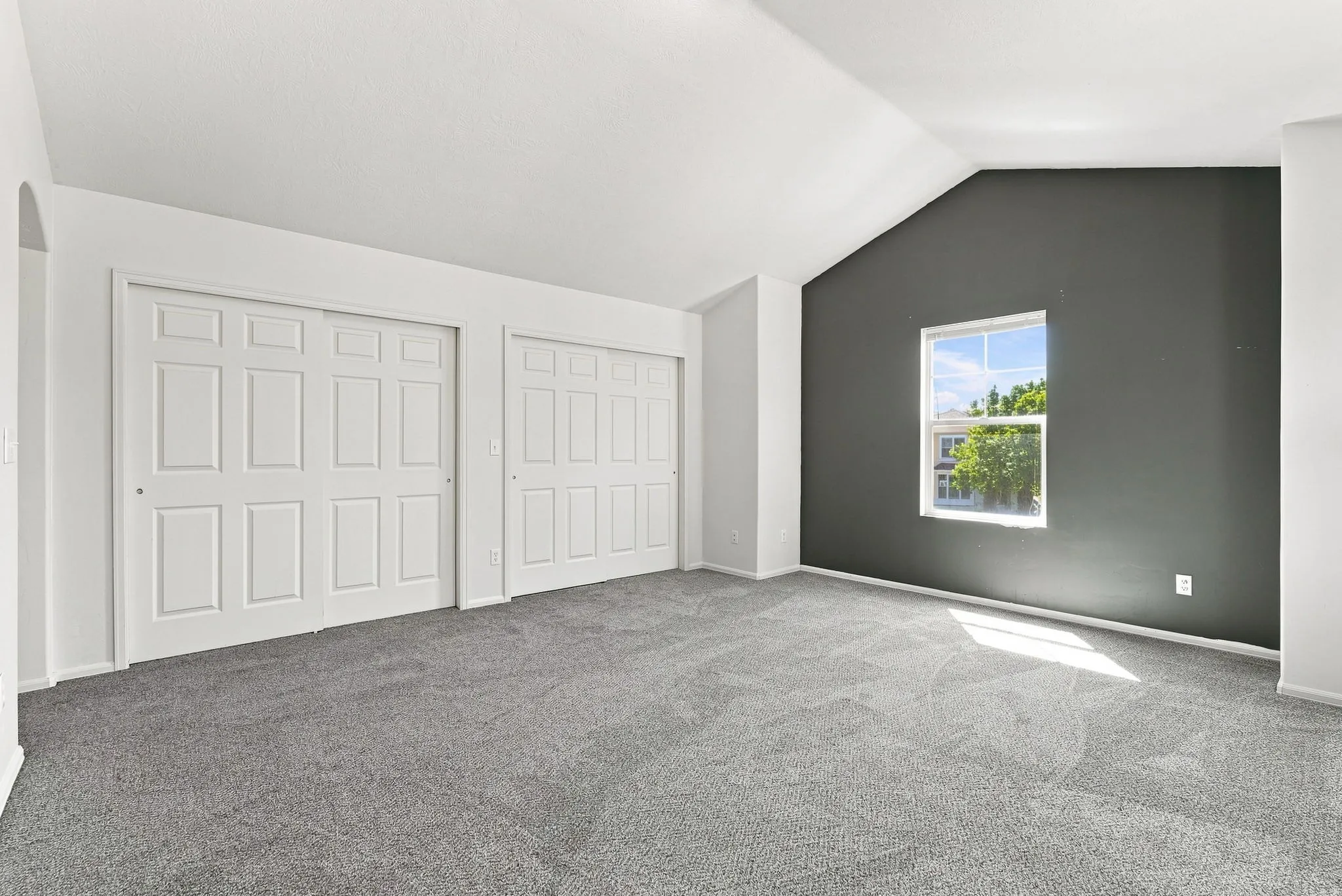 Vaulted ceiling, two paneled sliding closet doors, gray carpet, and a framed window