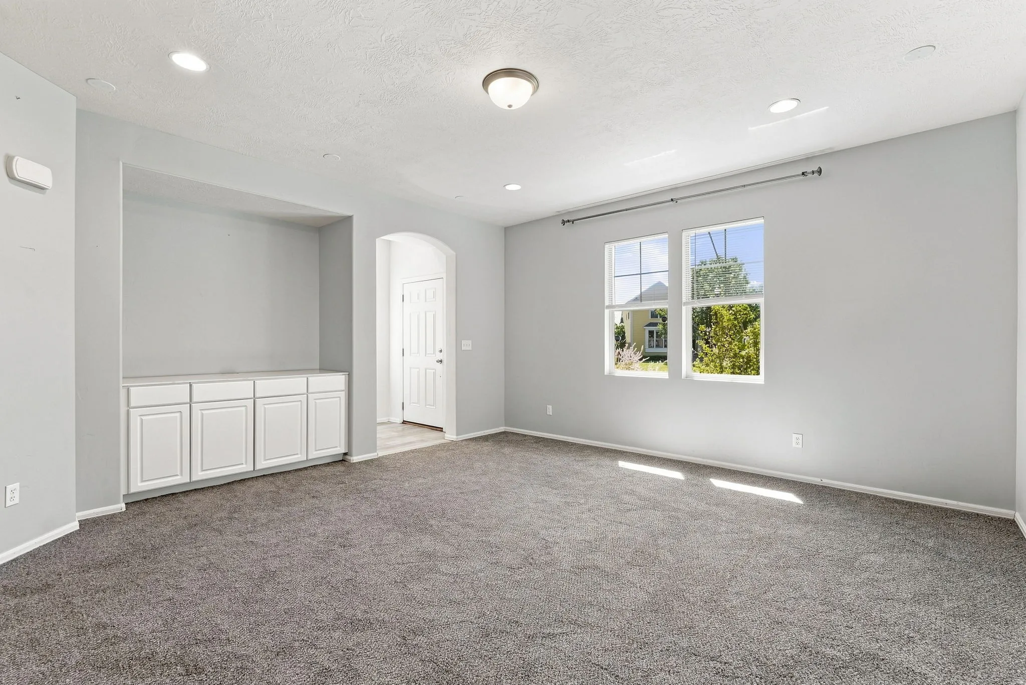 Expansive room featuring recessed lighting, a built-in media console with storage, a large window, and an arched entryway