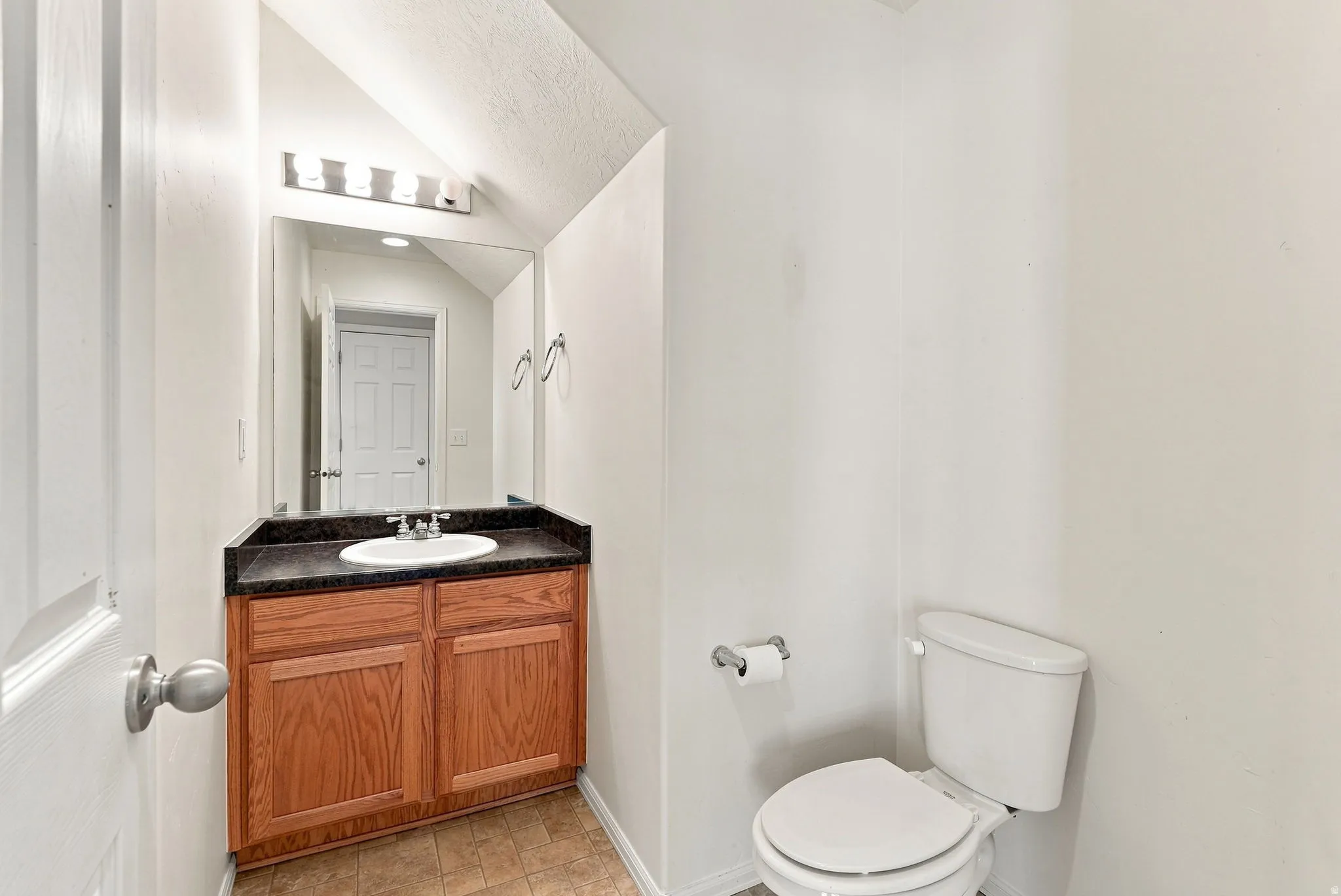 Wood-finish vanity with a surface-mounted sink, dark countertop, and rectangular mirror