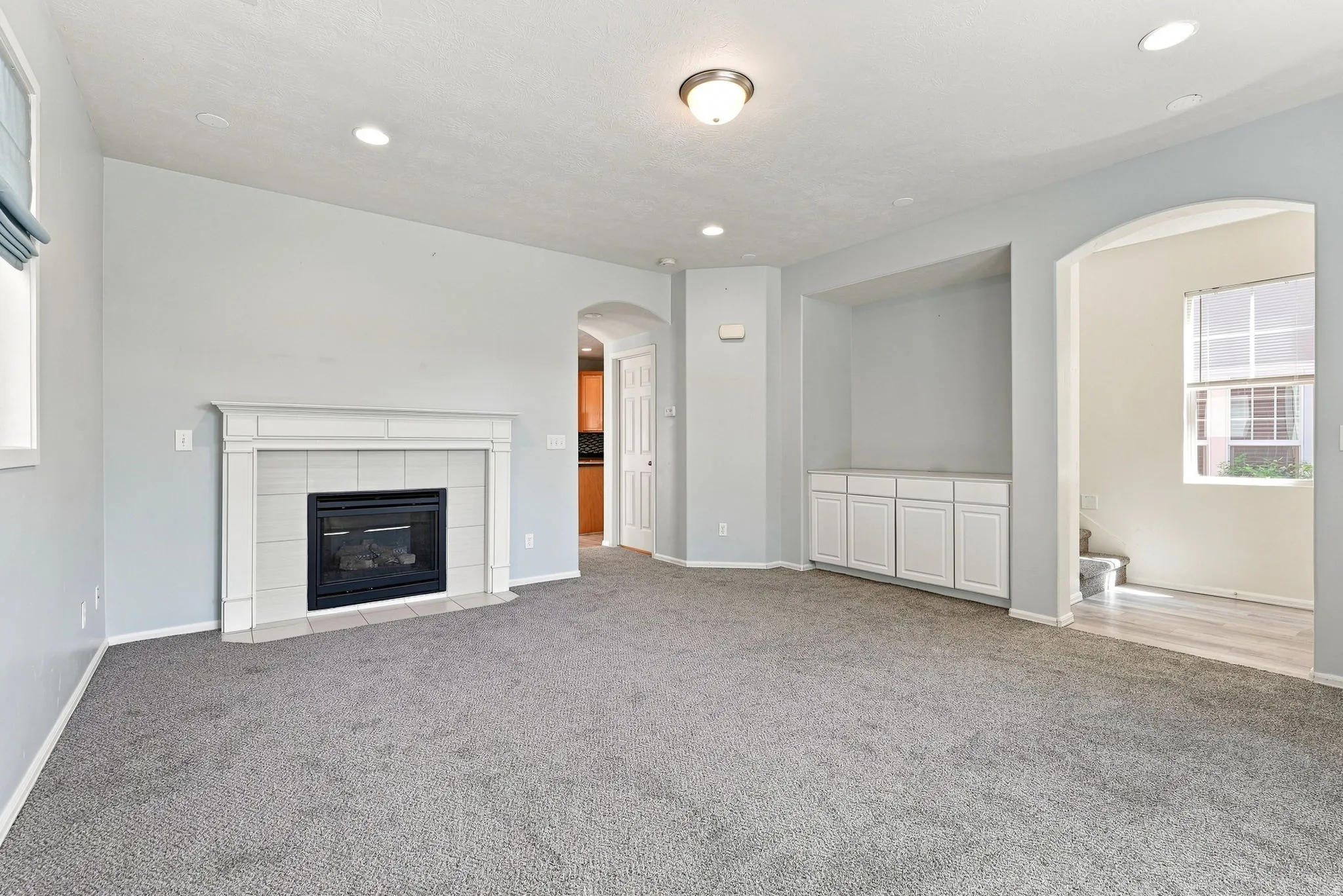 Recessed lighting, arched doorway, built-in cabinetry, fireplace with tiled surround, and neutral wall paint