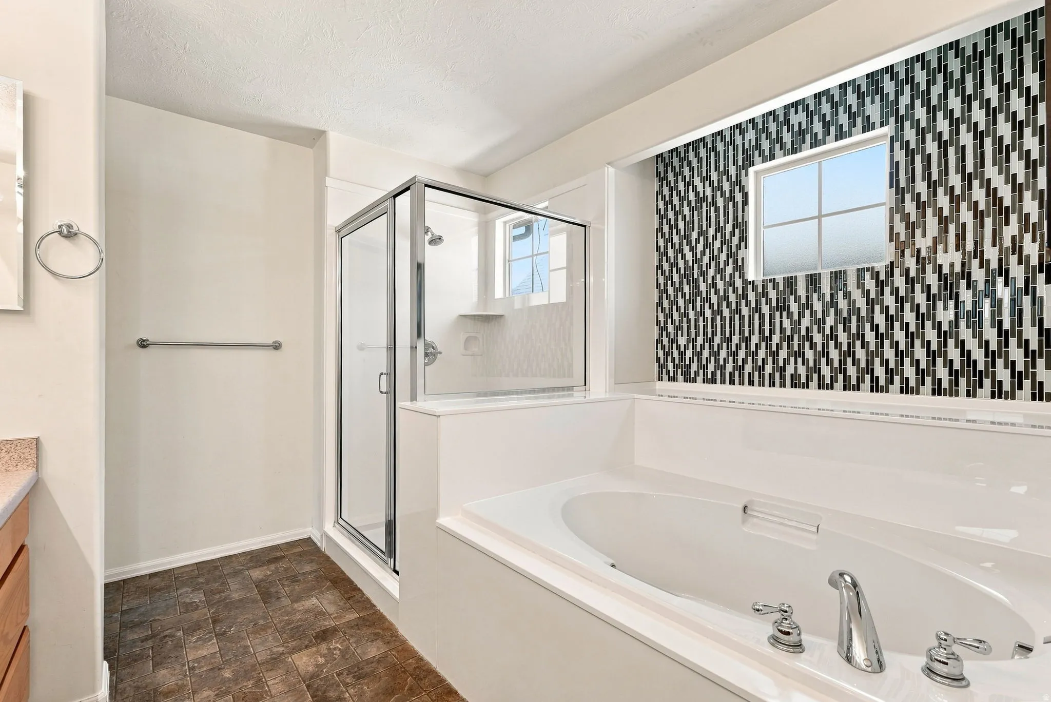 Integrated shower and soaking tub combination with a glass-enclosed shower, wall-mounted showerhead, and mosaic tile accent wall