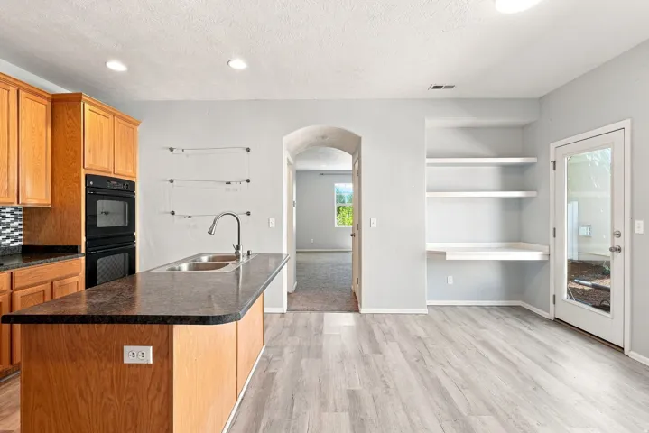 Kitchen featuring wood cabinetry, stainless steel double basin sink, double wall ovens, and a patterned tile backsplash