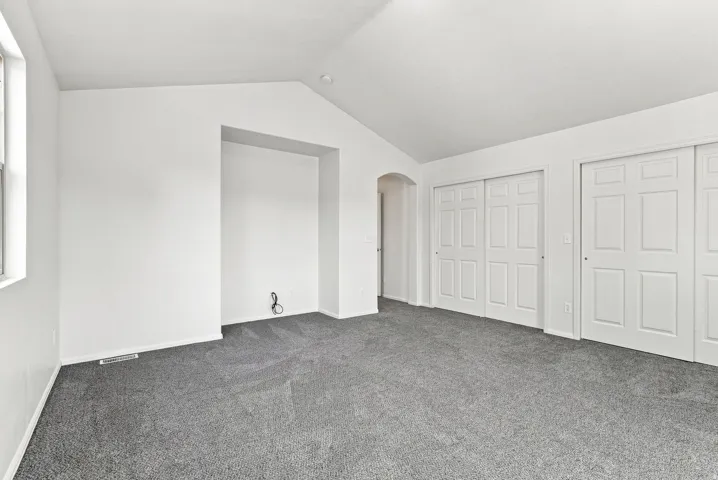 Vaulted ceilings, neutral carpet flooring, recessed wall niche, arched doorway, and white panel sliding closet doors
