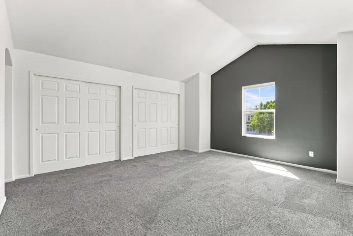 Vaulted ceiling, two paneled sliding closet doors, gray carpet, and a framed window