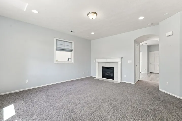 Wall-mounted window treatment, built-in fireplace with white mantel and dark tile surround, recessed lighting, ceiling-mounted light fixture, and archway with wood-finish flooring