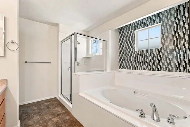 Integrated shower and soaking tub combination with a glass-enclosed shower, wall-mounted showerhead, and mosaic tile accent wall