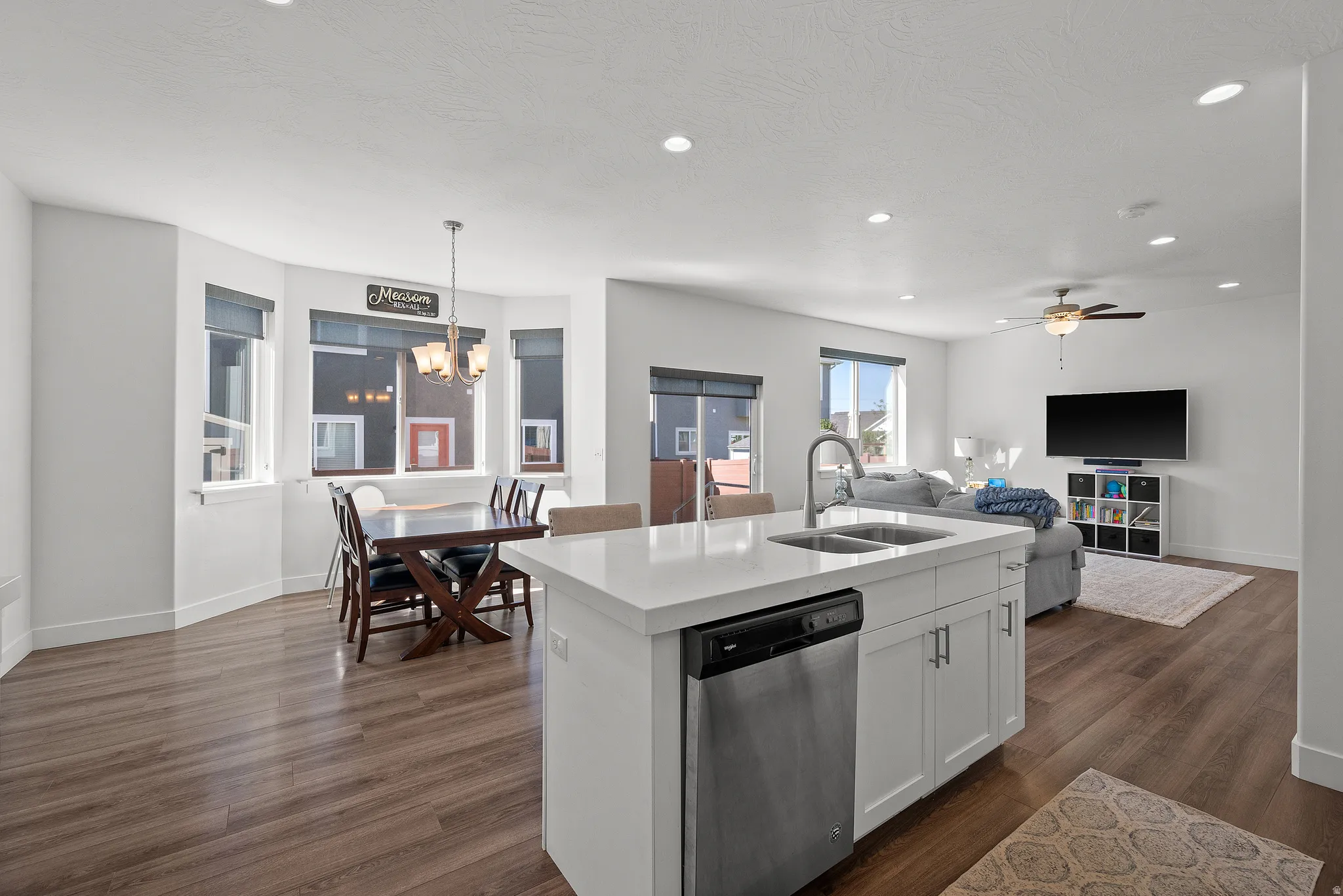 Open-concept living space with wood-finish flooring, recessed lighting, and a modern kitchen island featuring an undermount double-basin sink