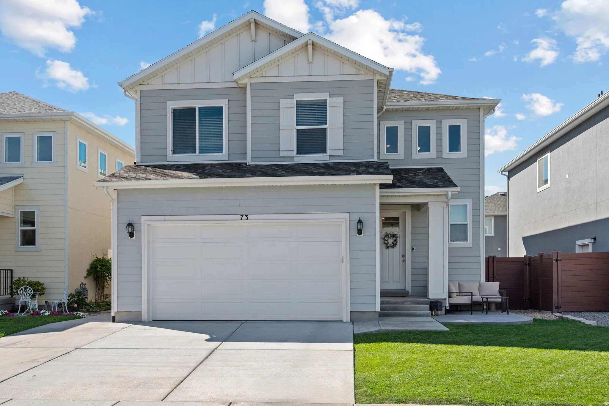 Contemporary two-story residence with light gray siding, white trim, attached two-car garage, concrete driveway, and a front patio