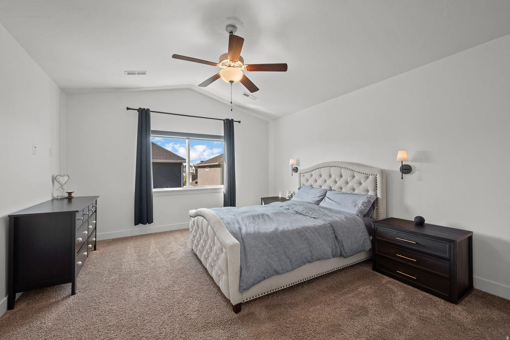 Vaulted ceiling with a ceiling fan, carpeted flooring, and a window with dark curtains