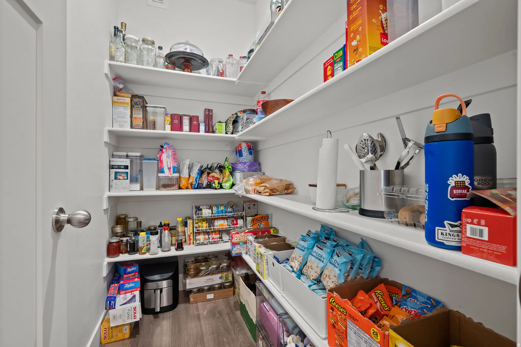 Walk-in pantry with extensive built-in shelving, wood-finish flooring, and a white paneled door