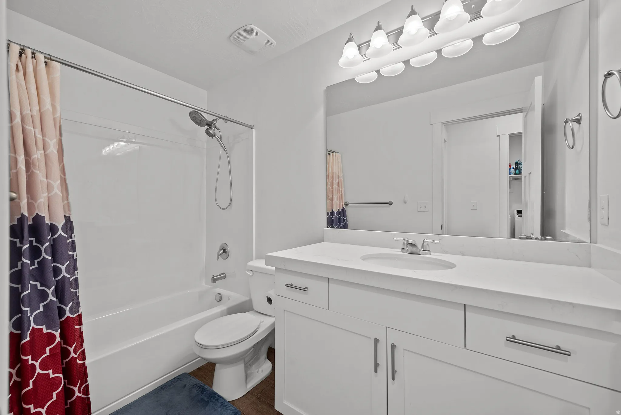 Bathroom featuring a white vanity with an integrated sink, polished chrome fixtures, a large mirror, and a white bathtub with a shower